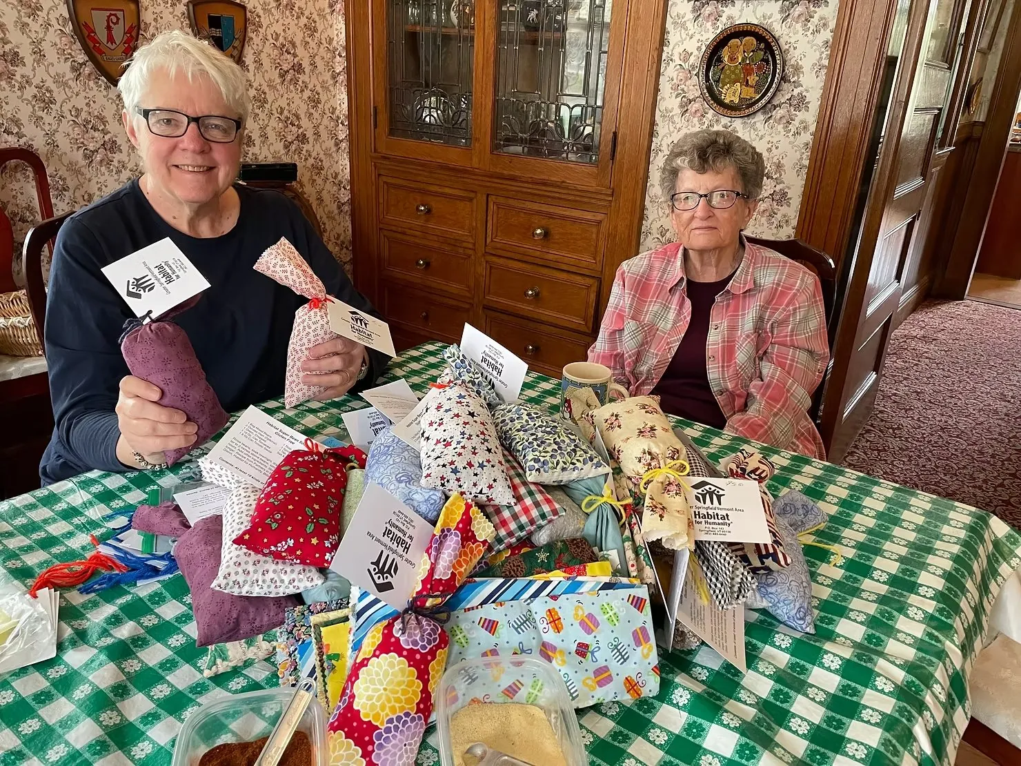 Two volunteers at a table covered with handmade Habitat Super Bean Soup mix packets tied with ribbon