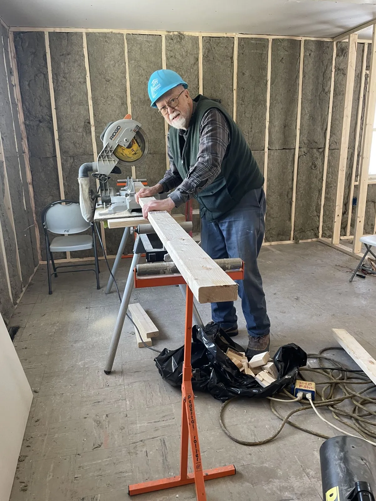 Volunteer in a hard hat cutting lumber with a miter saw