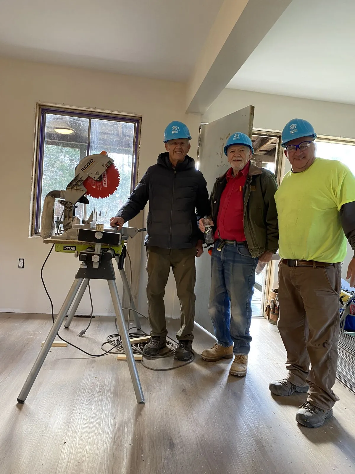 Three volunteers beside a miter saw in a home with newly installed flooring