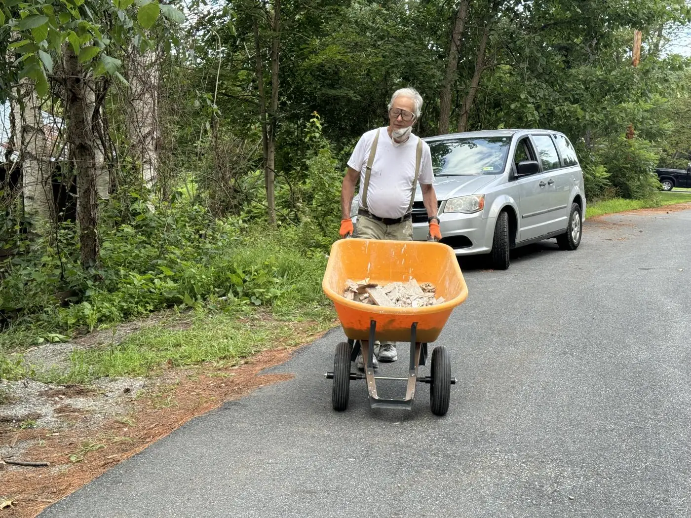 Volunteer pushing a power wheelbarrow loaded with debris along a neighborhood road