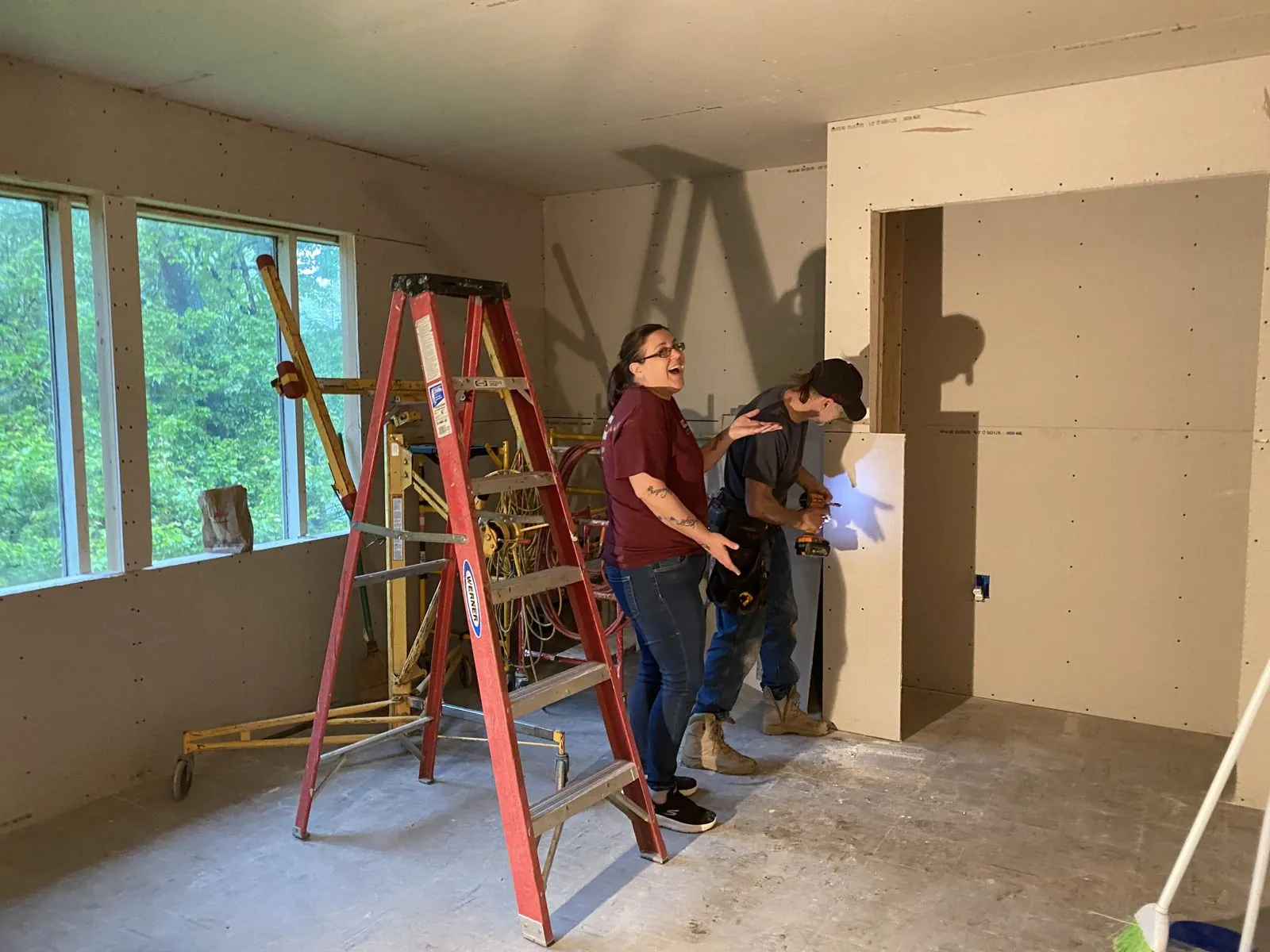 Two volunteers hanging drywall beside a ladder during a home renovation